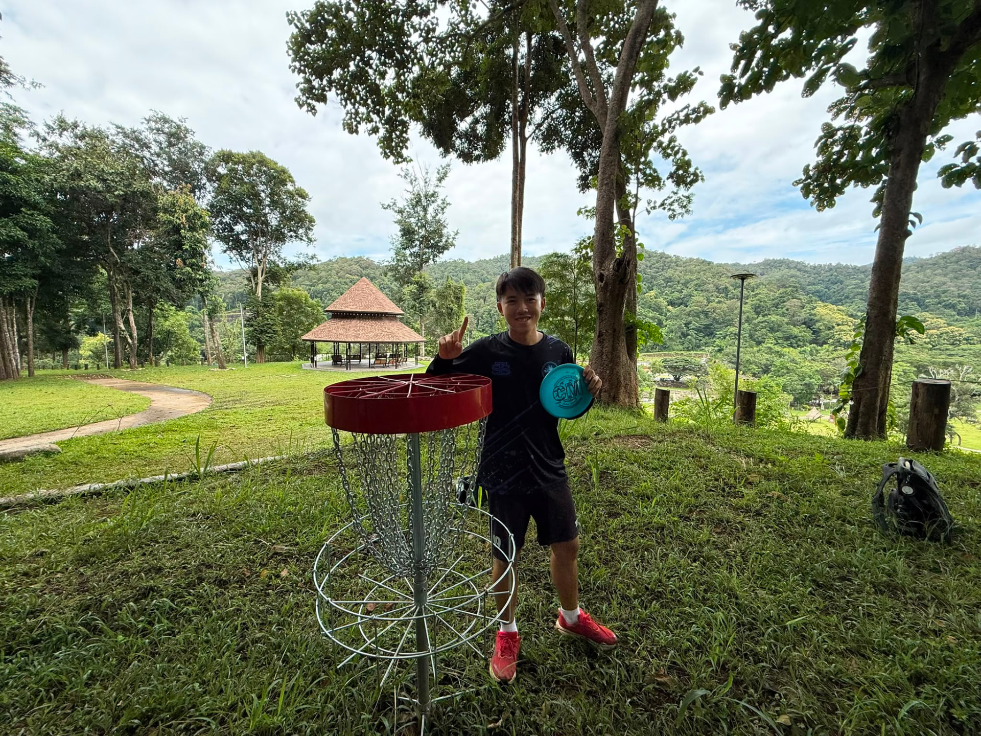 A young player holding a disc beside a red basket with a sala and mountains behind at Rock n' River