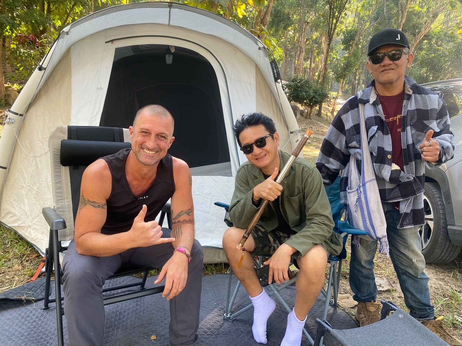 Campers relaxing in chairs outside their tent under the trees at Rock N River